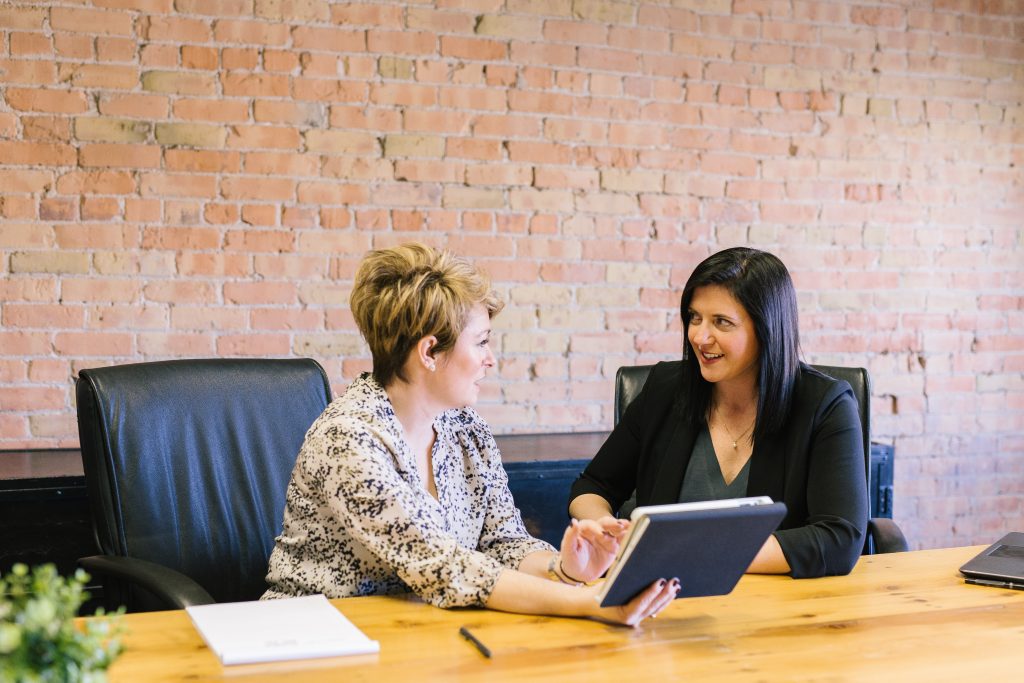 Two women sitting at a conference table discussing how to hire a dating coach.