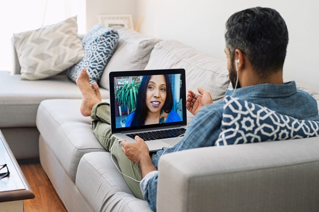 Man sitting on his couch having a virtual date night with his girlfriend.