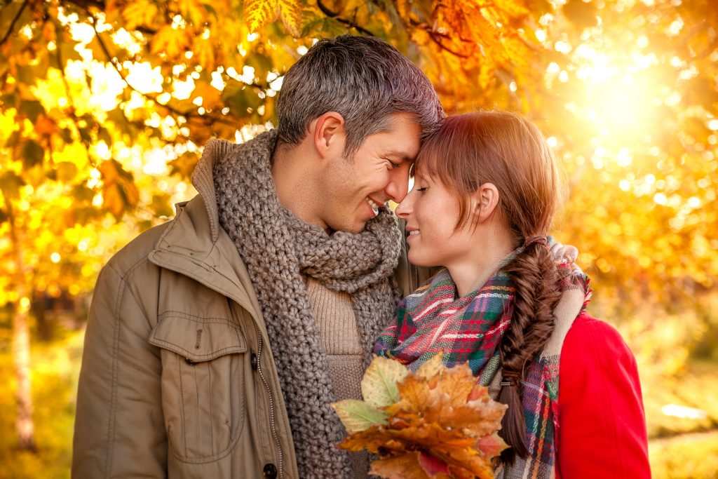 Man and woman hugging in a forest filled with fall foliage.