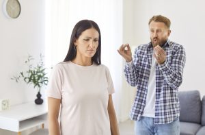 A sad woman wondering why she is always attracting toxic people, is facing away from an angry man who is yelling at her.
