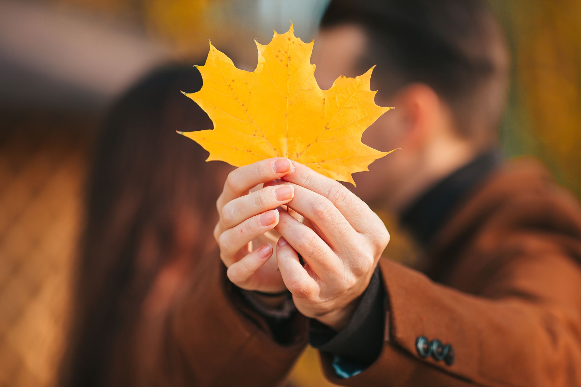 A couple kissing behind an autumn leaf who applied the fall online dating tips to find love.