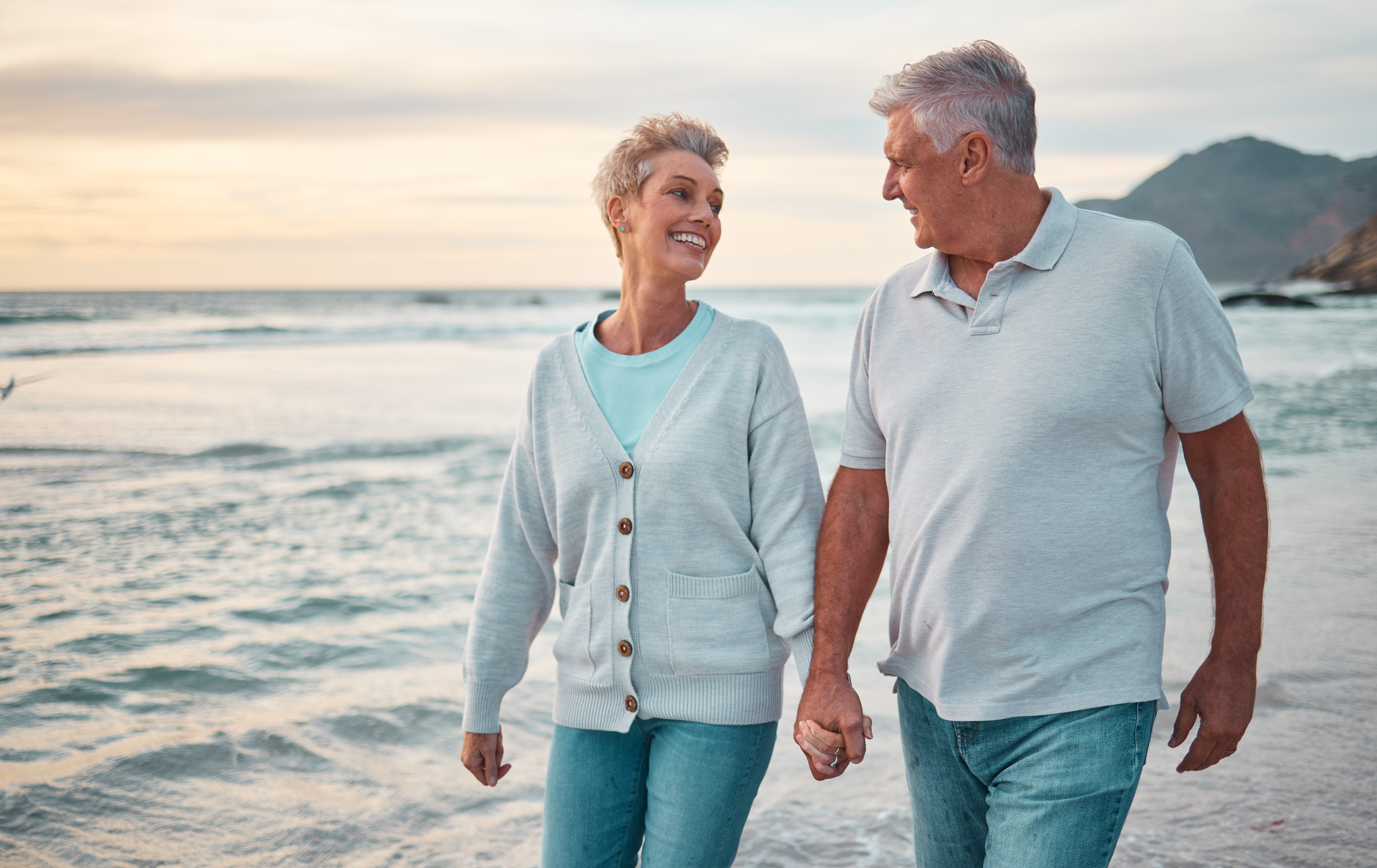 A couple in love, who each possess the qualities of a good partner, holding hands and walking on the beach at sunset.