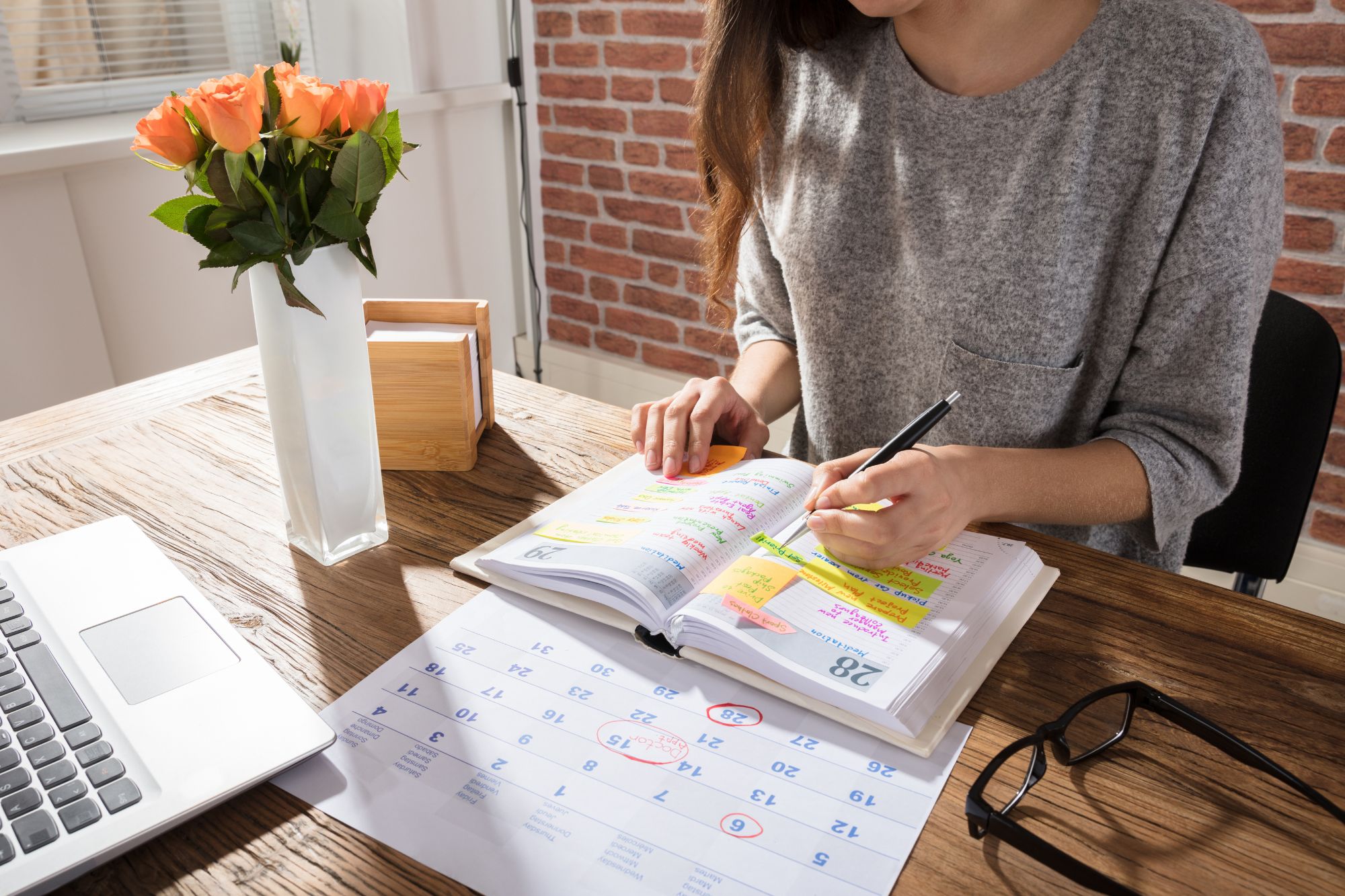 Woman at desk looking over her very full yearly/weekly calendar.