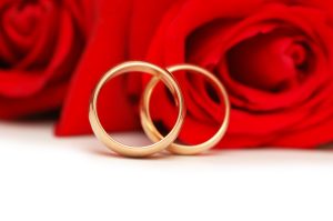 Close of 2 gold wedding bands on a backdrop of red roses- winning gold in olympic dating.