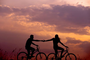 Couple riding bikes and holding hands at sunset.