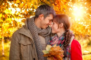 Man and woman hugging in a forest filled with fall foliage.