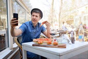 Man eating a pizza alone and taking a selfie.