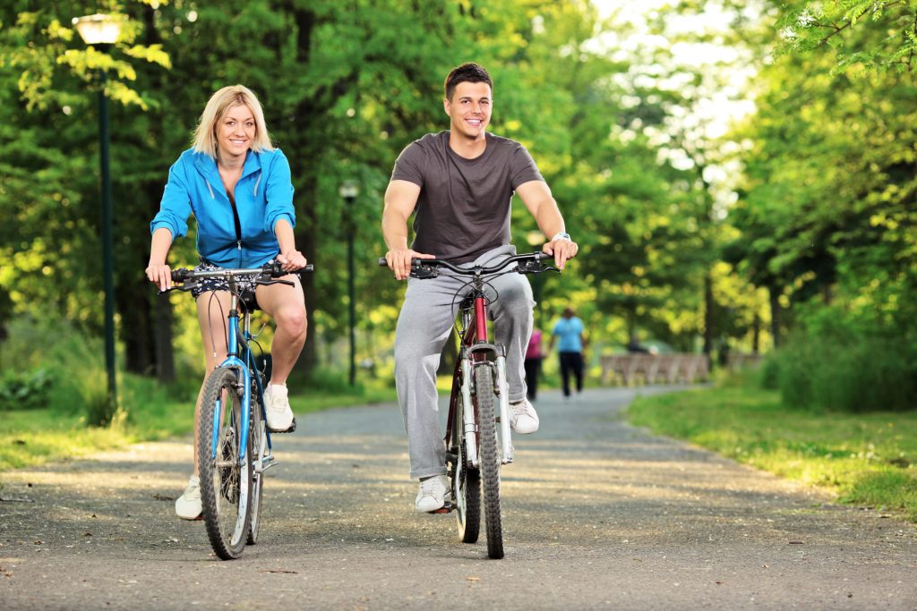 Couple riding bikes together on a pathway in a park.