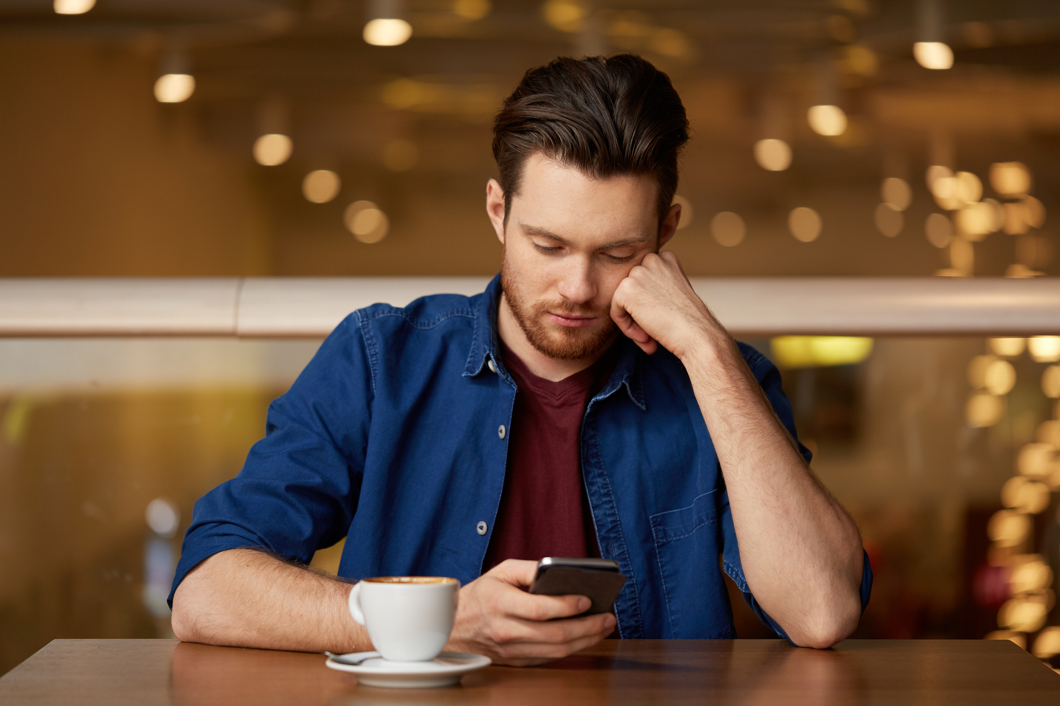 Man staring dejected at his phone as he struggles with his self-esteem.