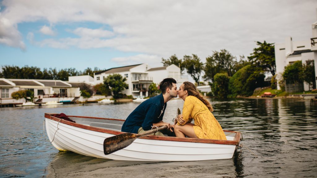 Couple in a rowboat gingerly leaning toward each other to kiss.