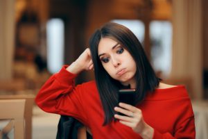 Exasperated woman looking at her phone and thinking online dating doesn't work.
