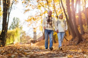 Senior couple walking hand-in-hand on a path strewn with colorful fall leaves.