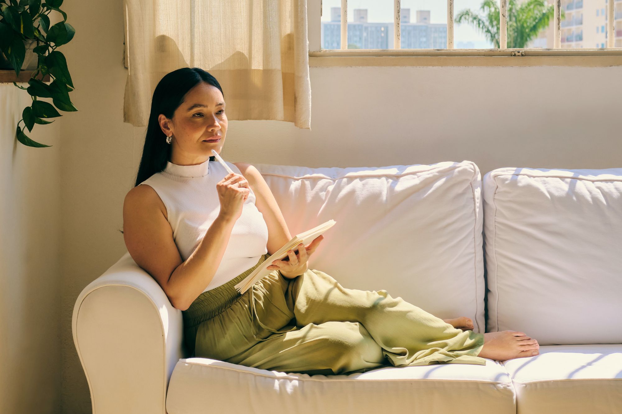 A woman sitting on her couch with a notebook and her pen to her lips, considering if she is truly prepared for love.